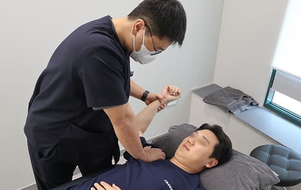 어깨 도수치료 장면 — 물리치료사가 가동 범위를 회복시키고 있다